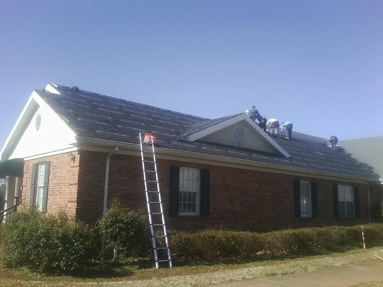 Crew tearing shingles off a brick ranch roof with a ladder set — Metal Roof Repair work by our crew in Marysville