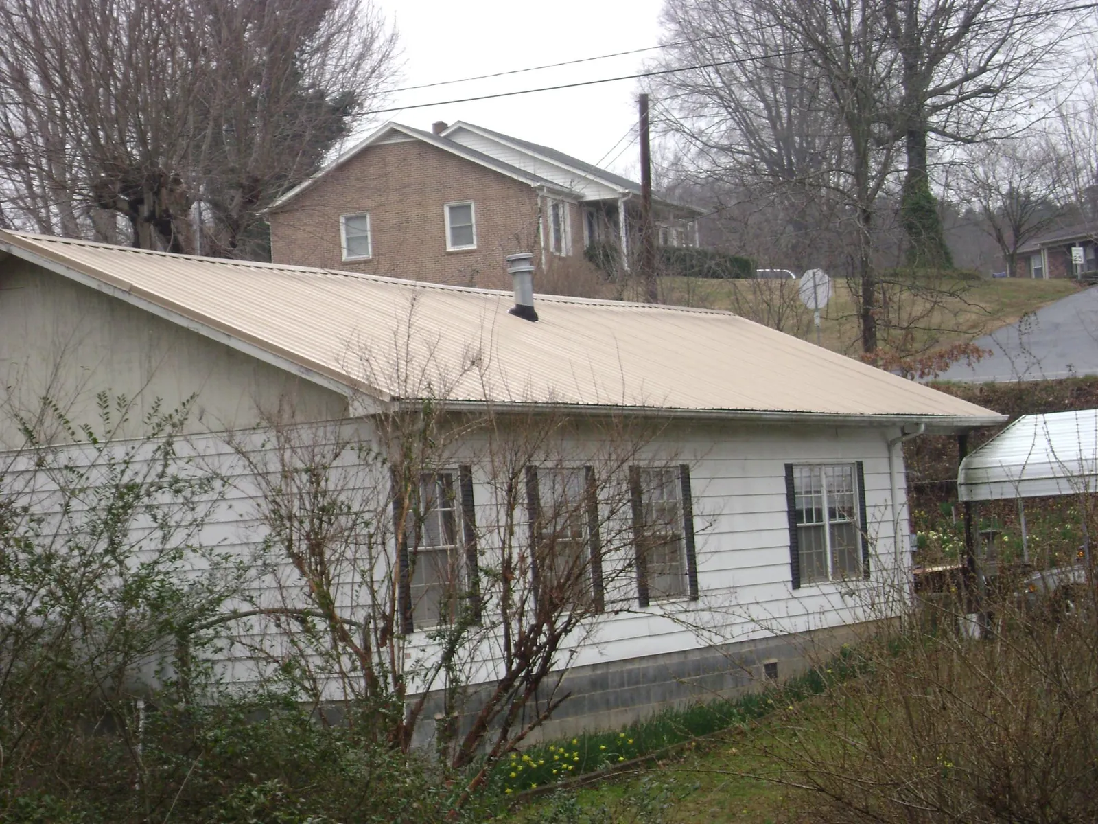 Tan metal roof on a white sided house set into a hillside — Commercial Roofing by Roofing Brothers in Marysville